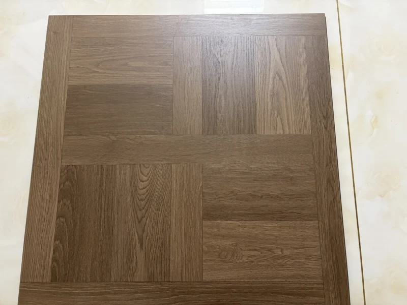 Close-up of a brown 600 × 600 mm wood-look LVT tile with a border and wood grain running in two directions.